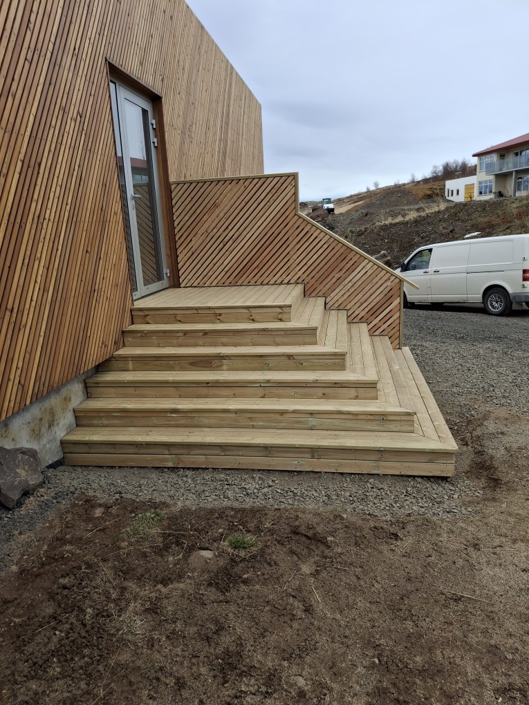 Breiðir timburstigar með skáklæddu handriði við timburklætt hús